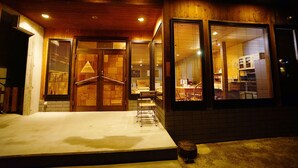 A building with a wooden exterior, large windows, and a visible interior with kitchen appliances. - HAKUBA Lodge OMUSUBI (Otari)