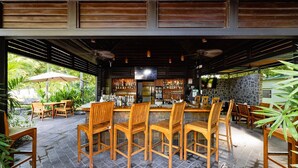 Un área de bar al aire libre con mobiliario de madera y un muro de piedra de fondo.