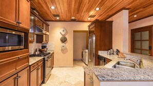 Una cocina moderna con armarios de madera, un microondas Bosch, un refrigerador de acero inoxidable, encimeras de granito y un lavamanos integrado.