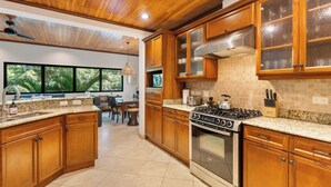 Una cocina moderna con armarios de madera, encimeras de granito, una estufa a gas y un ventanal con vistas a un jardín.