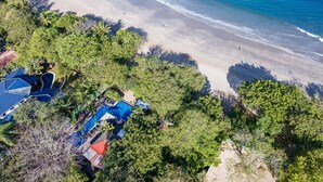 Vista aérea de un complejo turístico con piscina, playa y abundante vegetación.