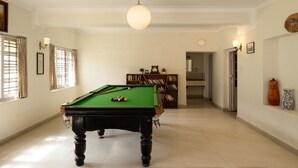 Una mesa de billar en una habitación bien iluminada con una estantería y un reloj en la pared.