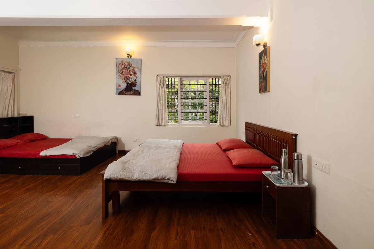 A bedroom with two beds, wooden flooring, a window with curtains, and wall-mounted lights.