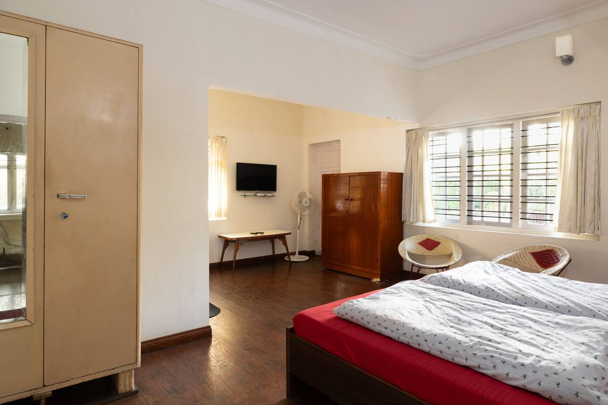 A bedroom with a bed, a wardrobe, a desk, a chair, and a television.