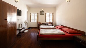Una habitación con una cama de madera, una pequeña mesa con sillas, un escritorio y un televisor fijado en la pared.