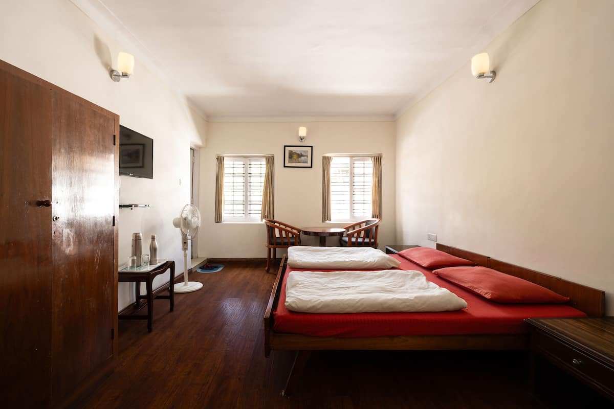 A room with a wooden bed, a small table with chairs, a desk, and a TV mounted on the wall.