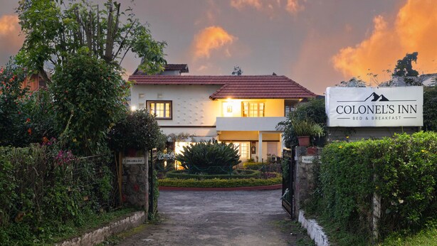 Un hotel llamado 'Colonel's Inn' con un letrero, entrada pavimentada y un jardín cuidado.