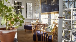 A room with a wooden floor, a table with chairs, a potted plant, and a painting on the wall. - Hotel Hornbækhus (Hornbaek)