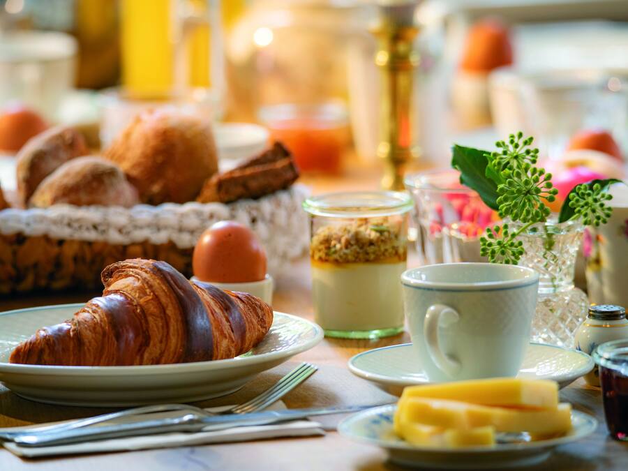 Una mesa de desayuno con croissants, una taza y un pequeño florero con una planta.