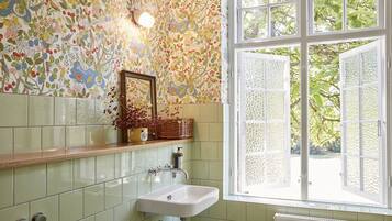 Un baño con papel tapiz floral, un lavabo blanco y una ventana con vistas a follaje.