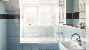 A modern bathroom with blue tiles, a bathtub, a sink, and a window.