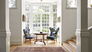 A bay window with multiple panes, wooden flooring, two chairs with floral upholstery, a round table, and a patterned rug. - Hotel Hornbækhus (Hornbaek)