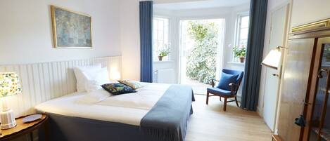 A bedroom with a bed, bedside table, lamp, chair, and a view of the outdoors.