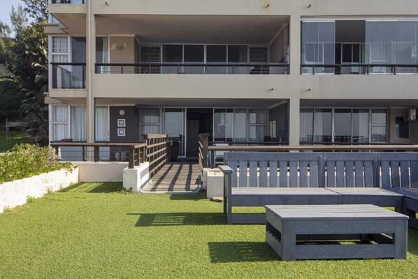 A modern multi-story building with a flat roof, large windows, and a small outdoor seating area with benches.