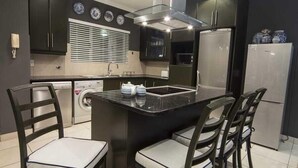 Une cuisine compacte avec des meubles de rangement sombres, un îlot central doté de tabourets, un four encastré et un réfrigérateur.