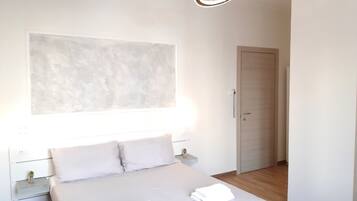 Quarto moderno com uma cama grande, mesas de cabeceira, uma obra de arte na parede e uma porta.