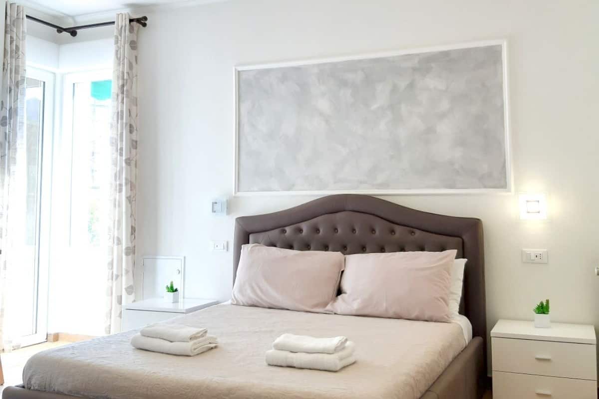 A modern bedroom with a large bed, a tufted headboard, a wall-mounted abstract painting, and a ceiling light fixture.