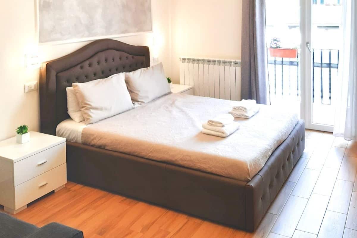 A modern bedroom with a large bed, a nightstand, a radiator, and a view of the outside.