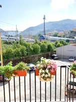 Un balcón con macetas y vistas a una estación de tren con trenes y edificios al fondo.