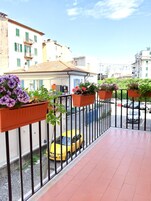 Un balcón con macetas de flores naranjas, un coche amarillo estacionado en la calle y edificios al fondo.