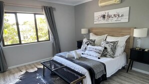 Une chambre à coucher comprenant un lit, des tables de chevet, un banc, une fenêtre avec des rideaux et un climatiseur fixé au mur.
