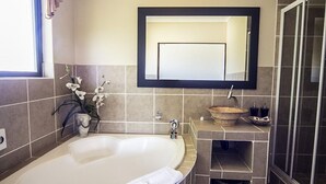 Une salle de bain moderne avec une grande baignoire, un lavabo agrémenté d’un récipient décoratif, un miroir et un espace douche.