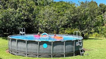 Piscina elevada redonda con escaleras a cada lado, rodeada de césped y abundante follaje.