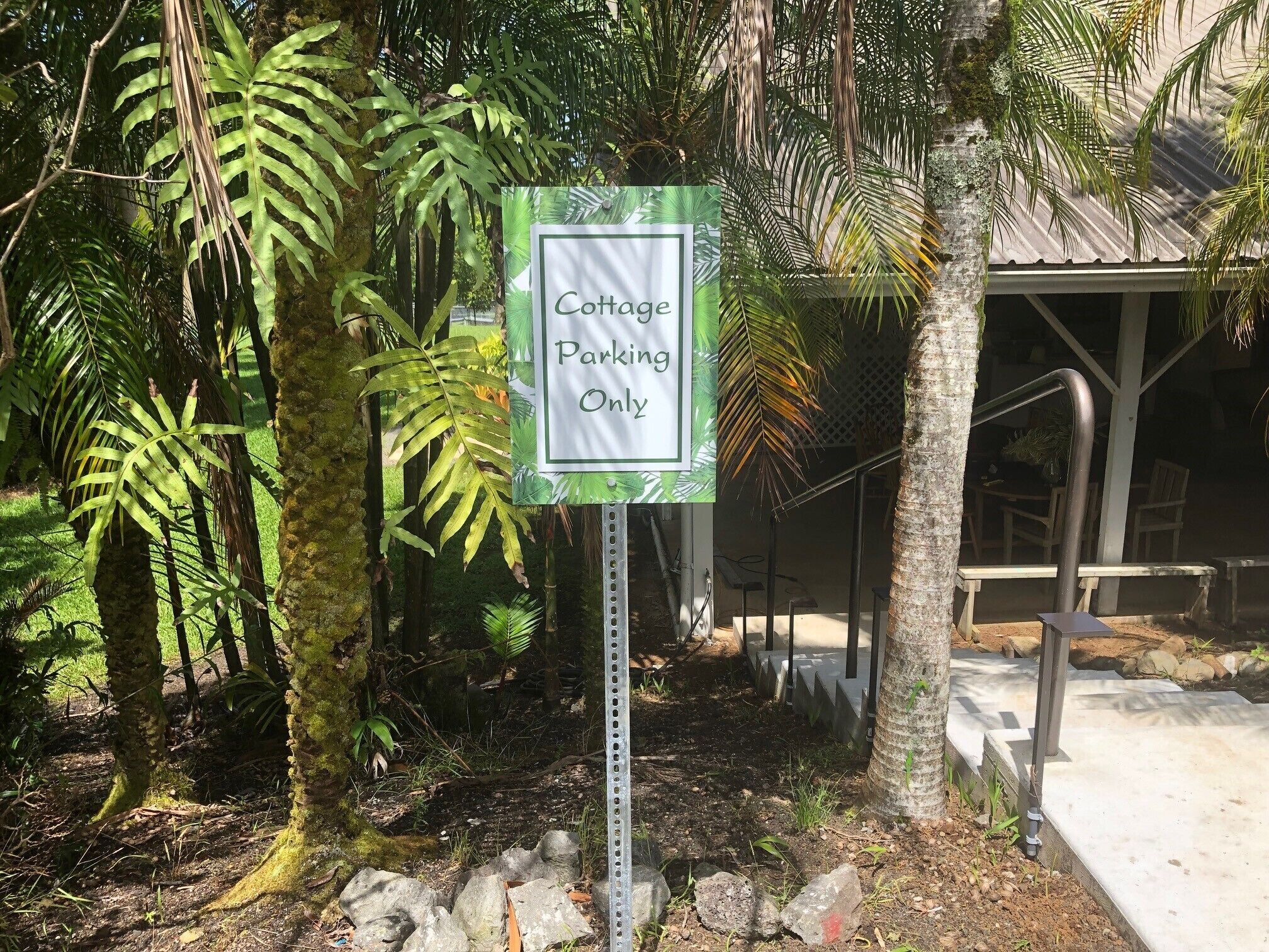 A sign indicating 'Cottage Parking Only' in a lush, green environment with a stone pathway and seating area.