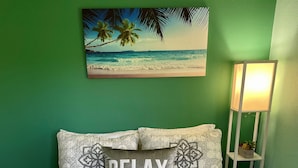 Ein Bett mit einem gemusterten Überwurf, ein Kissen mit dem Wort "RELAX" und ein Strandbild an der Wand.