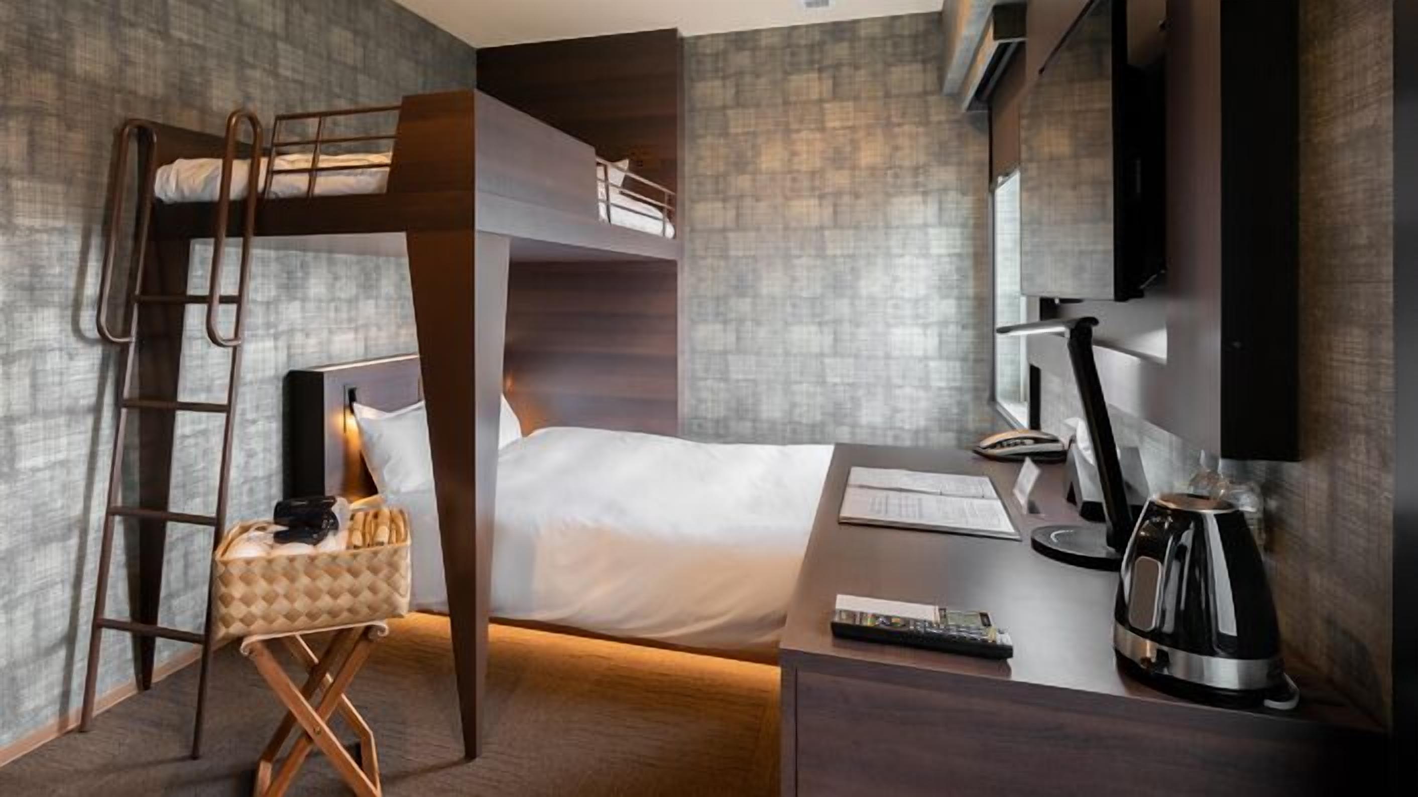 Habitación de hotel moderna con literas, un escritorio con computadora, una cafetera y un televisor.