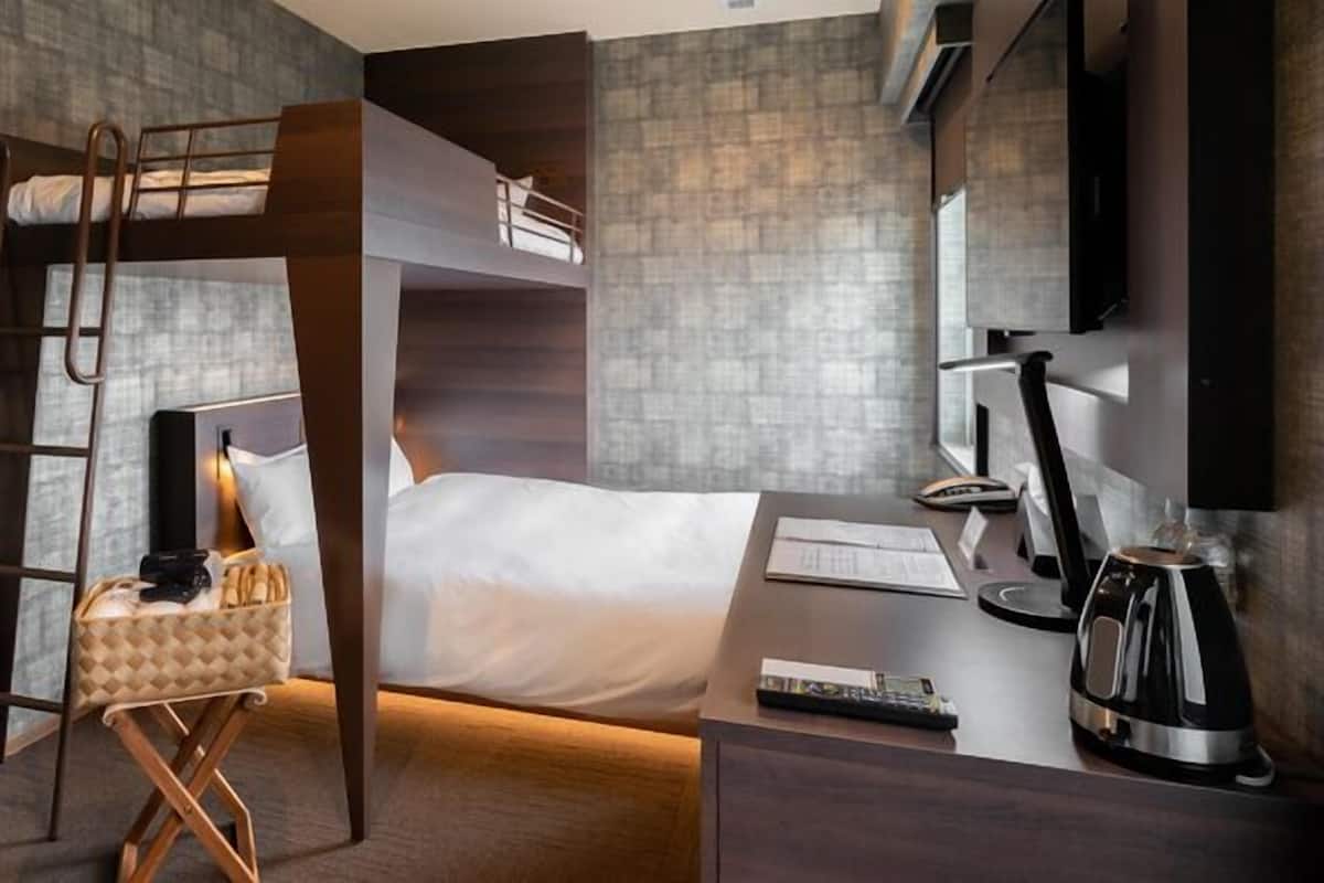 Moderni hotellihuone, jossa on kerrossänky, työpöytä tietokoneella, kahvinkeitin ja televisio.
