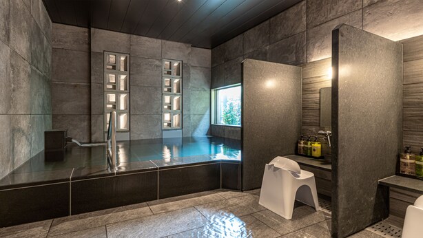 Ein modernes Badezimmer mit einer großen Badewanne, einem kleinen Hocker und einem Fenster mit Tageslicht.