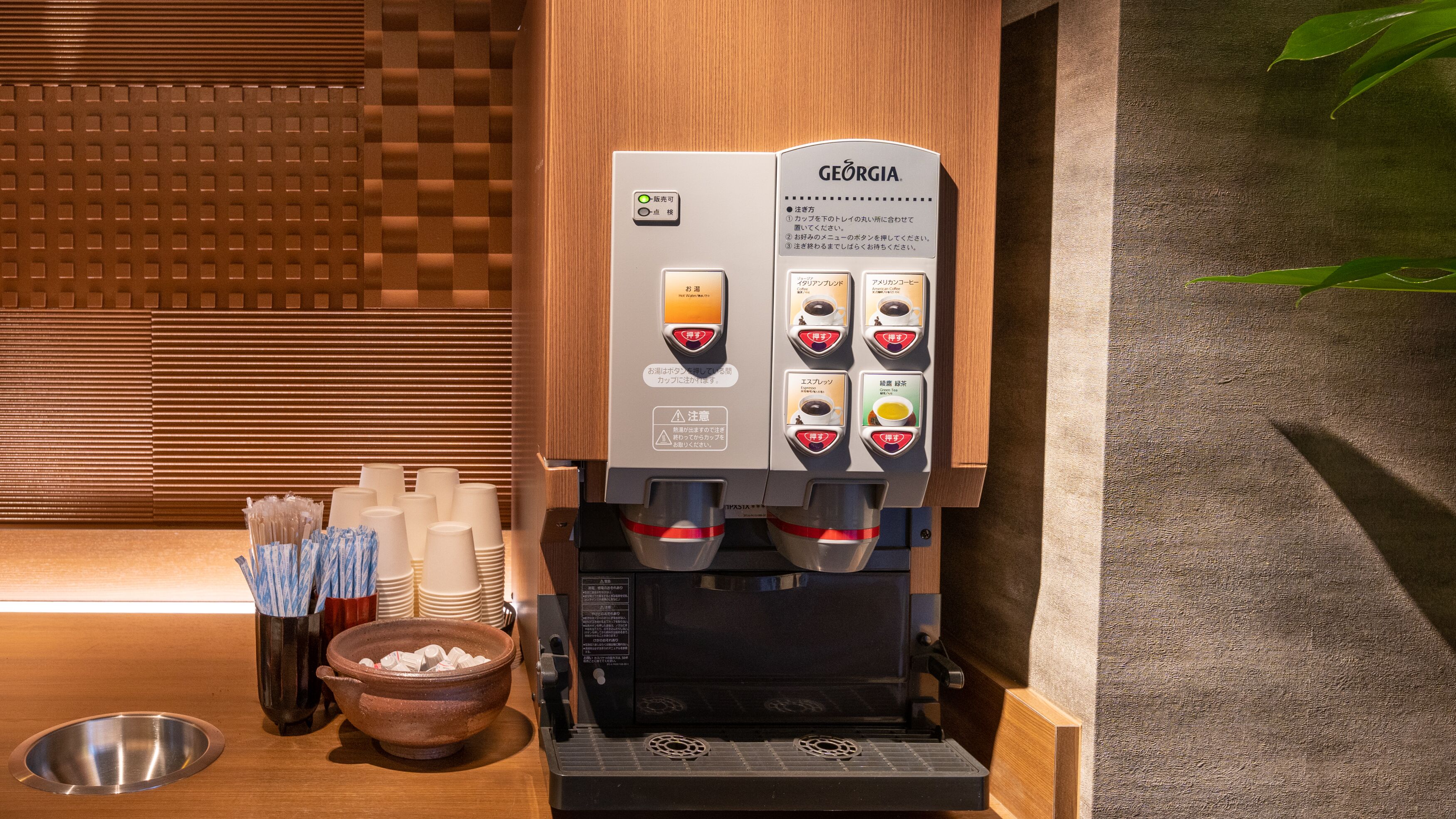 A coffee machine with multiple buttons and a water dispenser, placed next to a bowl of sugar cubes and a metal bowl.