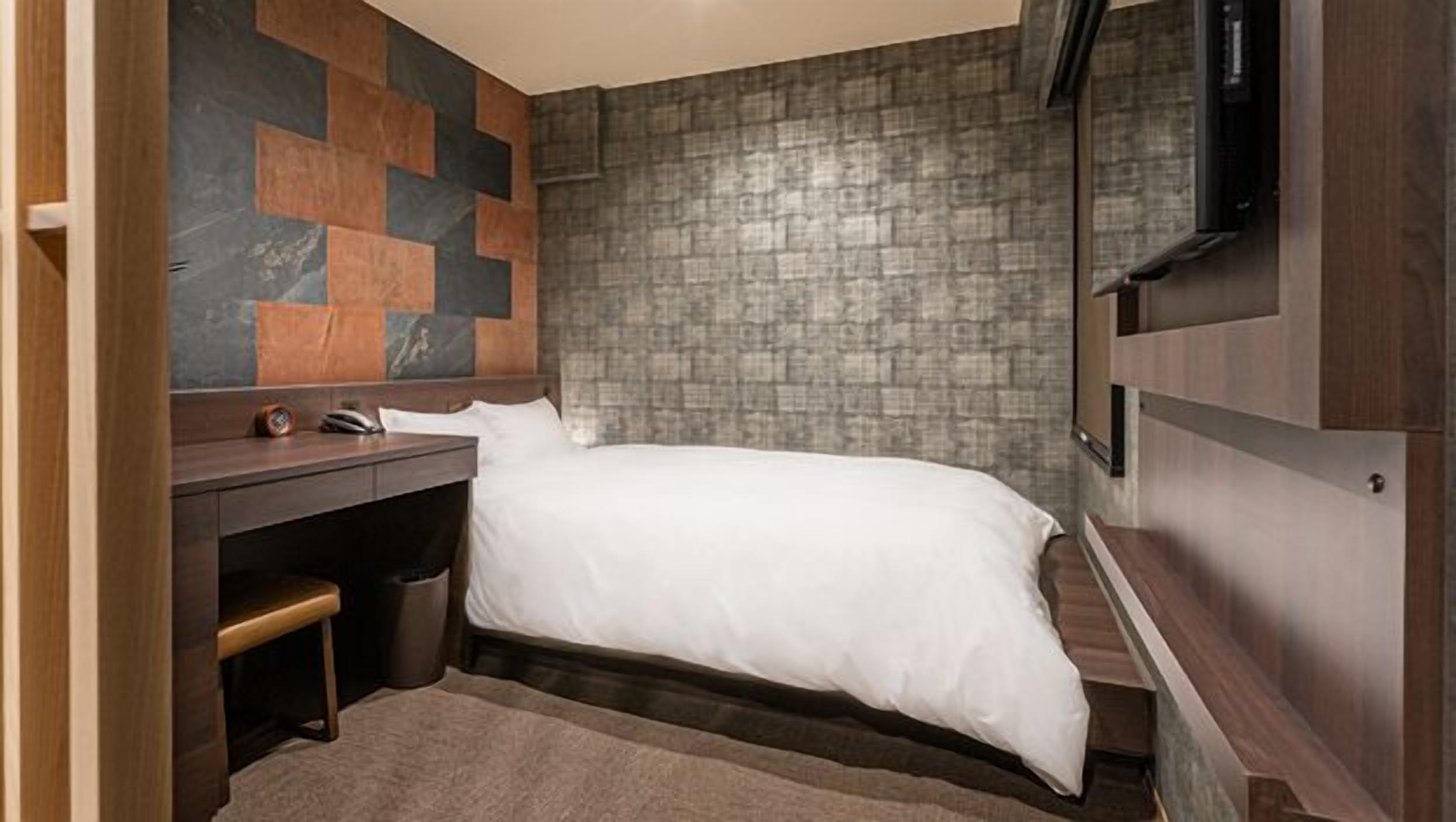 A bedroom with a bed, a desk, and a TV.