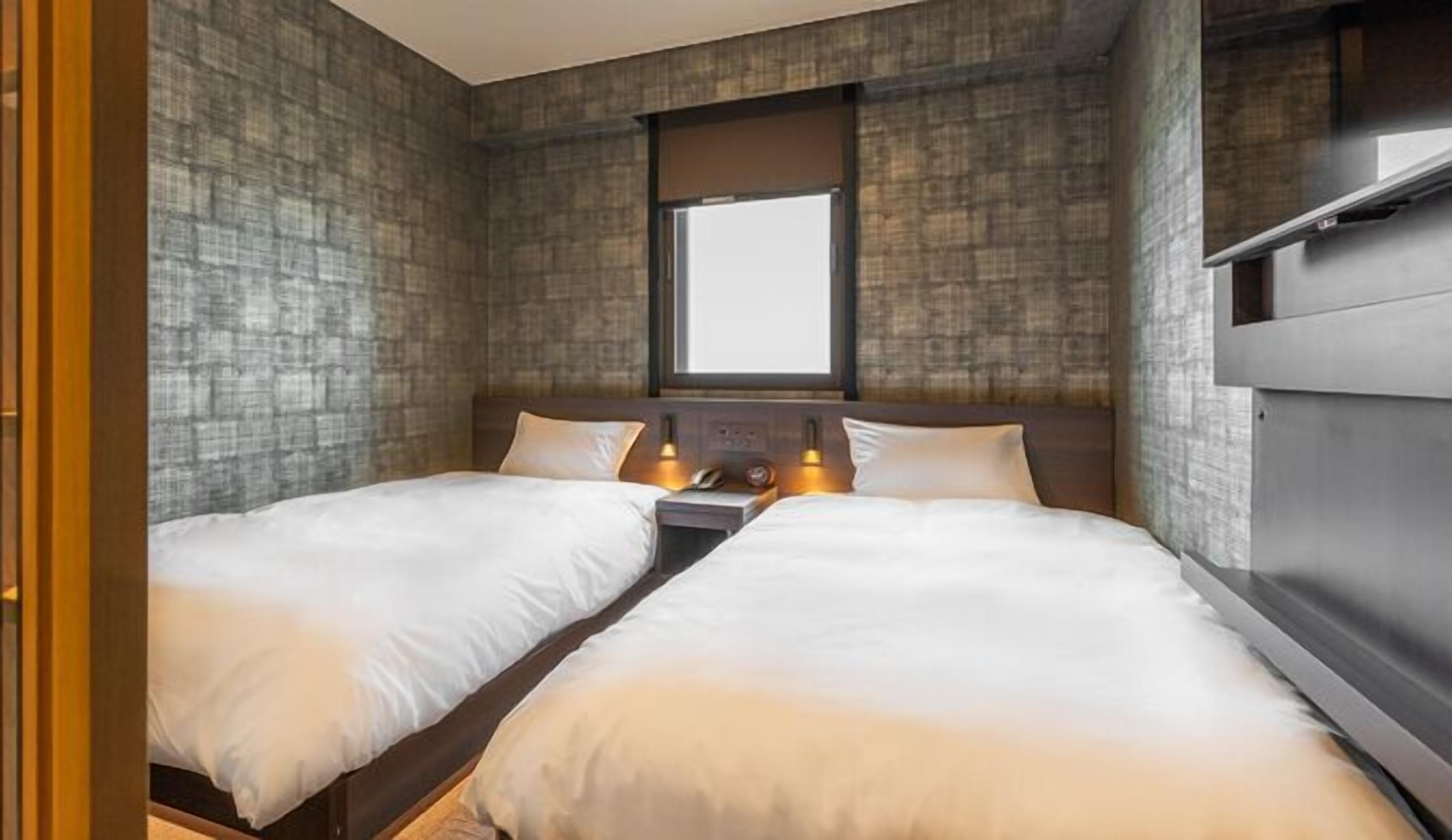 A room with two beds, a window, and a built-in shelf.