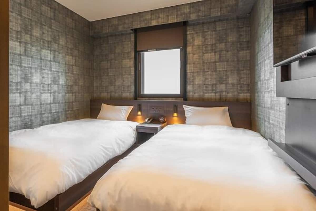 A room with two beds, a window, and a built-in shelf.
