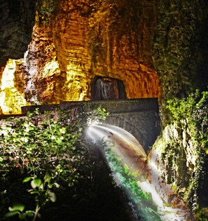 Une grotte avec une cascade et des parois illuminées.