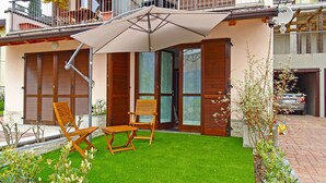 A house with a patio, two wooden chairs, a table, and a large umbrella. - La Quiete 24 Holideal Apartment Lake view (Tremosine)