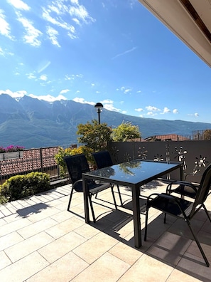 A terrace with a table and chairs, a lamp, and a view of mountains.