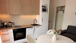 Une cuisine moderne avec des meubles en bois, un four à micro-ondes, une machine à café et un coin repas comprenant une table et des chaises blanches.