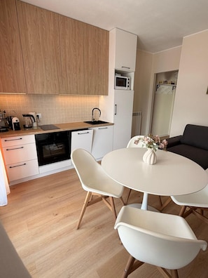 A modern kitchen with wooden cabinets, a microwave, a coffee maker, and a dining area with a white table and chairs.
