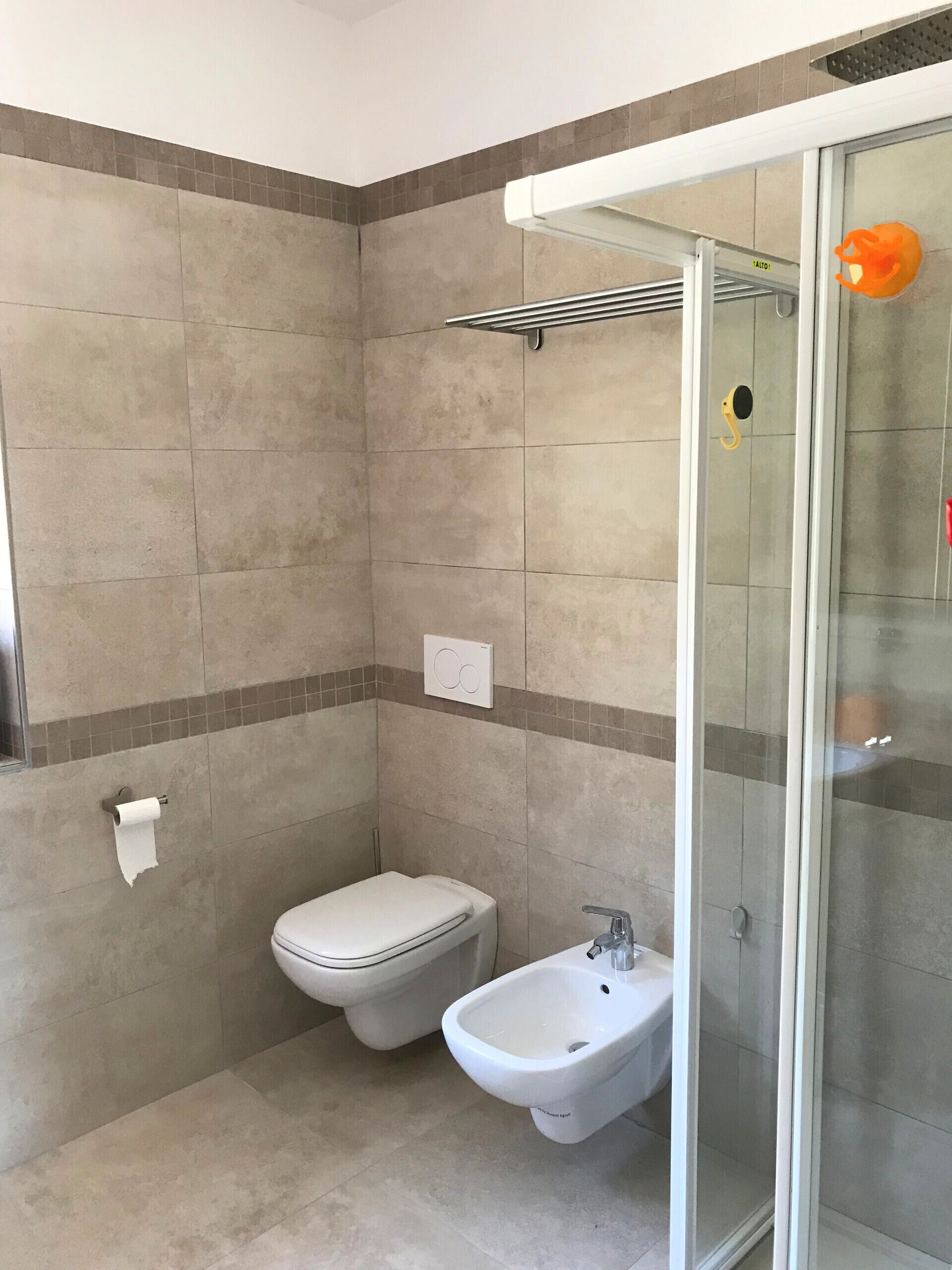 Et badeværelse med toilet, bidet og brusekabine i glas.
