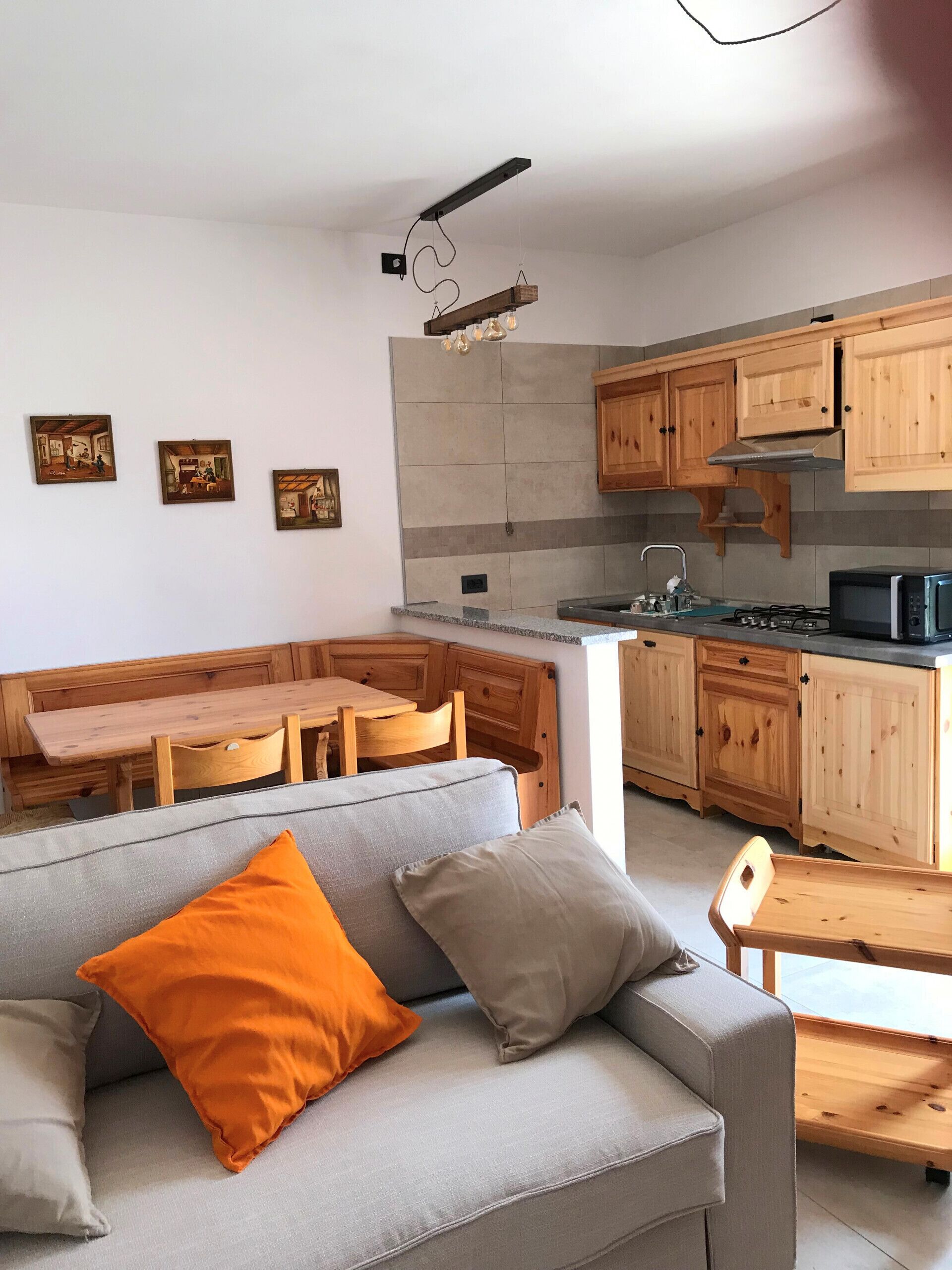 Una cocina moderna con armarios de madera, horno empotrado y una zona de comedor con sofá gris y cojín naranja.
