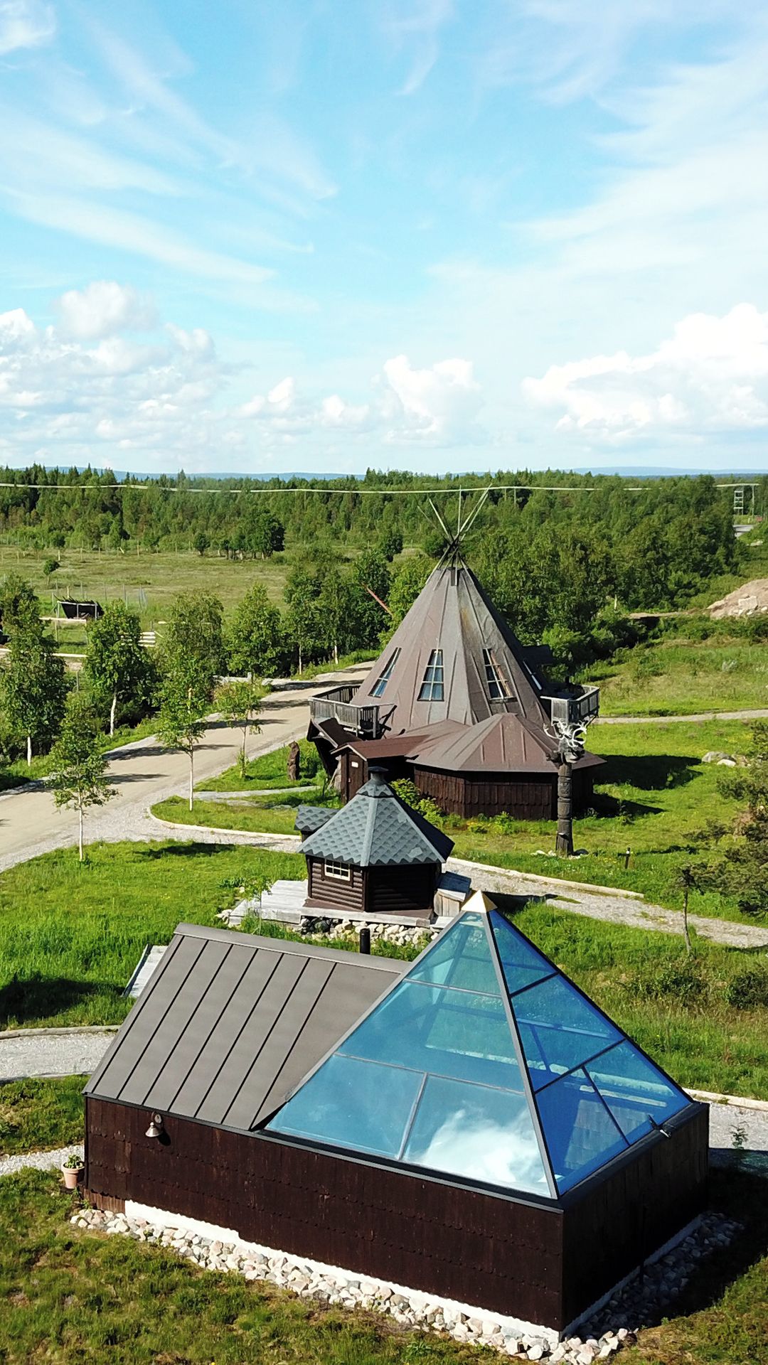 A modern building with a conical roof, surrounded by a lush green landscape.