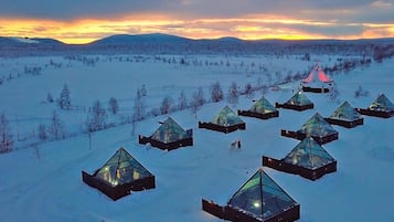 Uma série de estruturas de vidro em formato de pirâmide em uma paisagem nevada ao pôr do sol.