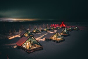 Una serie de cabañas piramidales con paredes de vidrio, ubicadas en un paisaje nevado durante la noche.