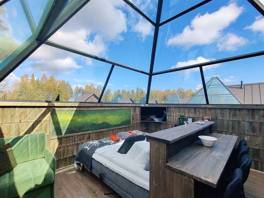 A modern, open-plan room with a glass ceiling, a bed, a small table, and a TV.