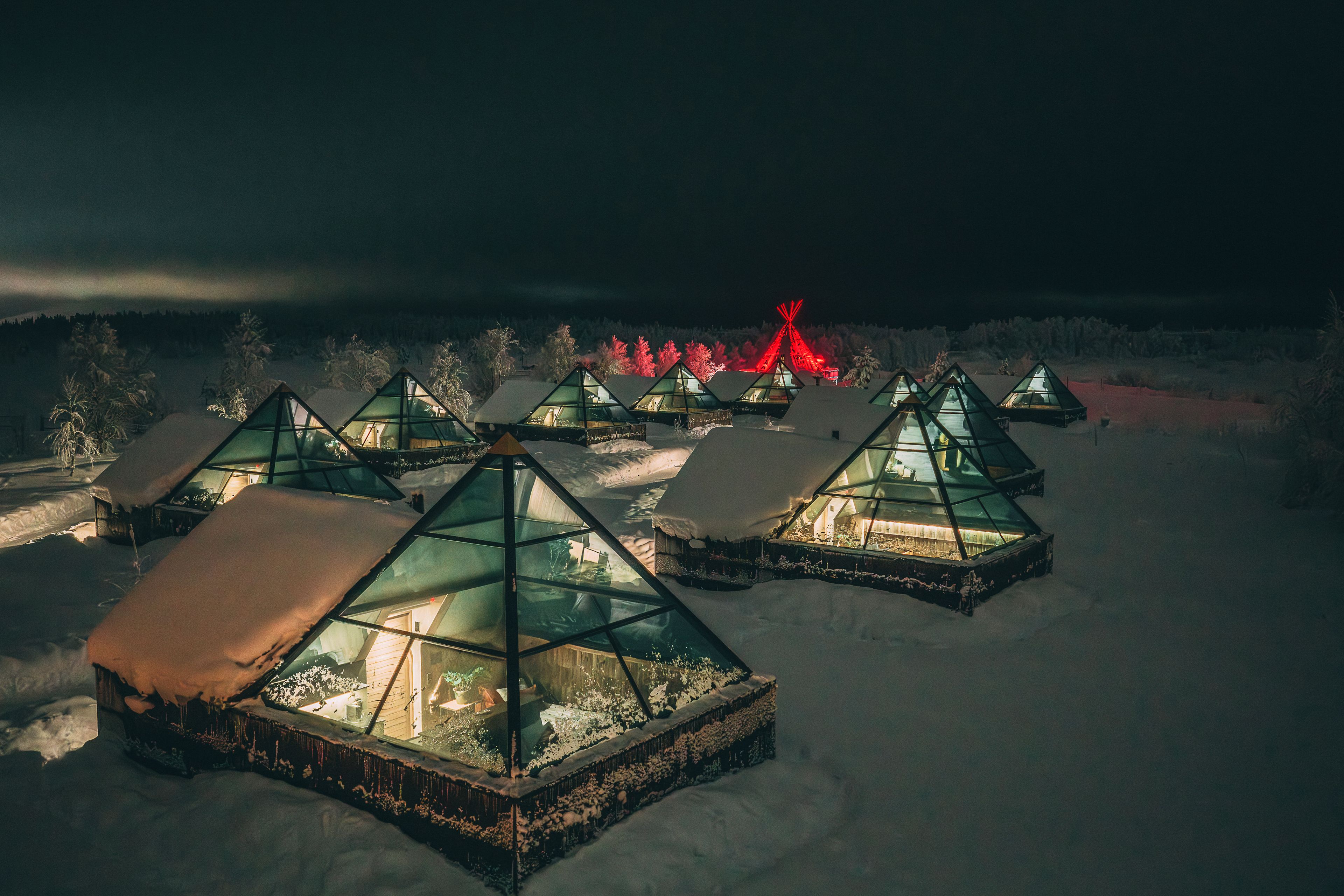 Una serie de estructuras geodésicas cubiertas de nieve con paredes de vidrio, ubicadas en un paisaje nevado de noche.