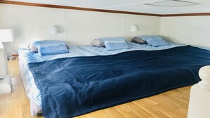 A bedroom with a bed, a nightstand, a lamp, and a wooden floor. - Mini Chula Inn (Chatan)