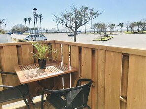 A wooden deck with a table and chairs, overlooking a parking lot with cars and palm trees. - Mini Chula Inn (Chatan)